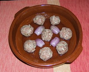 Uncooked meatballs and shallots in a terracotta pan