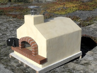 The Toscan wood fired pizza oven by Forno Bravo shown with a gabled roof and tuscan glaze on the stucco.