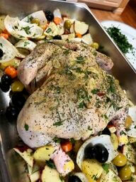 Uncooked chicken with herbs and spices on a bed of vegetables in a silver pan