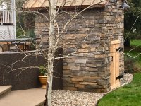 View of Side and Rear of a Casa110 Pizza Oven in the Craftsman Style - Stone Enclosure - Copper Roof - Cedar Door - Aspen Tree in Foreground