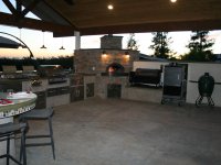 Covered, Open Air Putdoor Kitchen Anchored with a Casa110 Pizza Oven in the Corner with a Fire Burning at Sunset