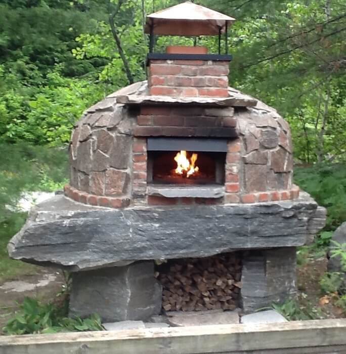 Dome-style Wood Fired Pizza Oven with Fire Burning Resting on a Large Granite Slab - Oven Finished with Natural Stone and Brick