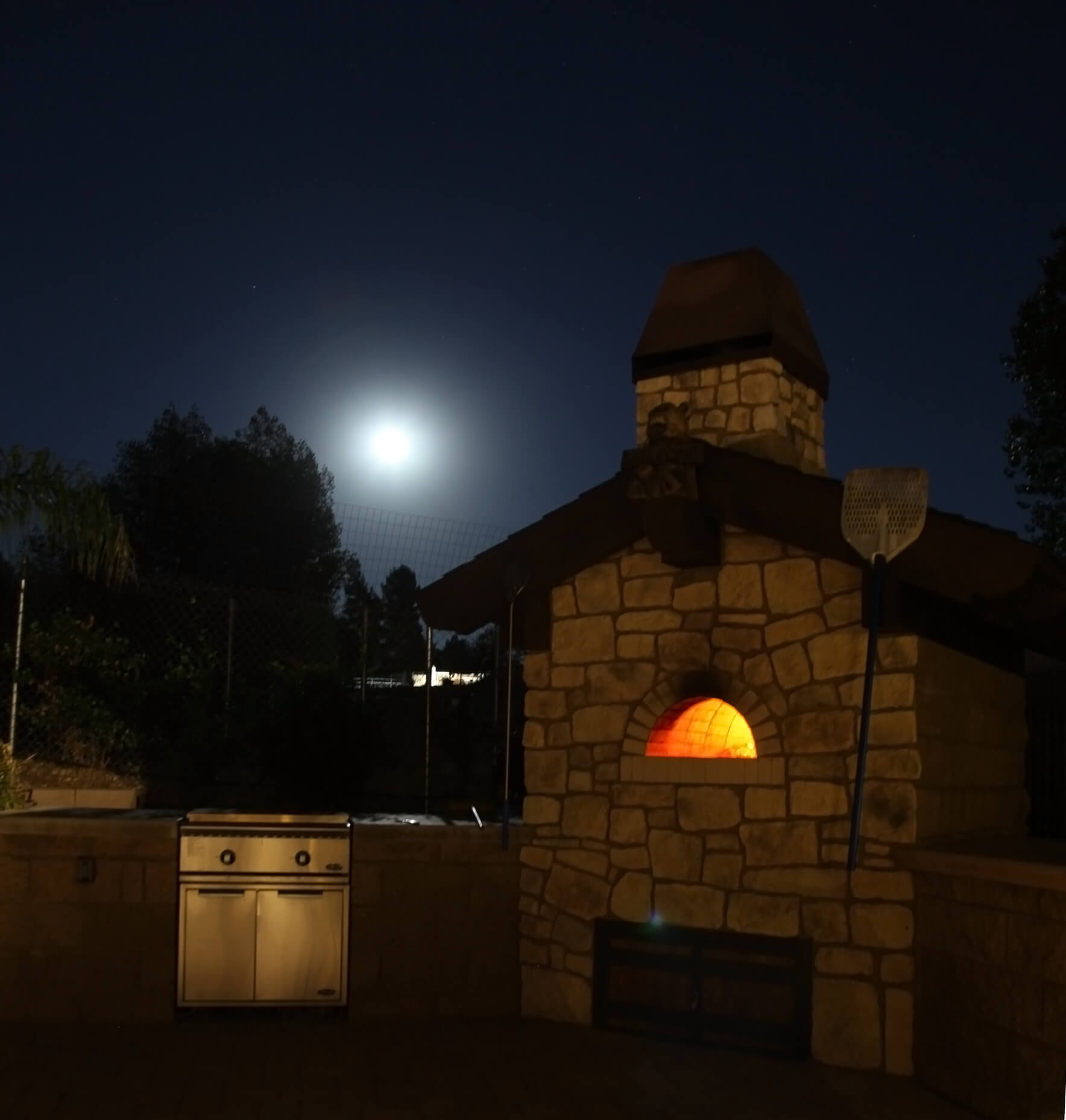 Outdoor kitchen with custom brick oven glowing orange under the light of the moon