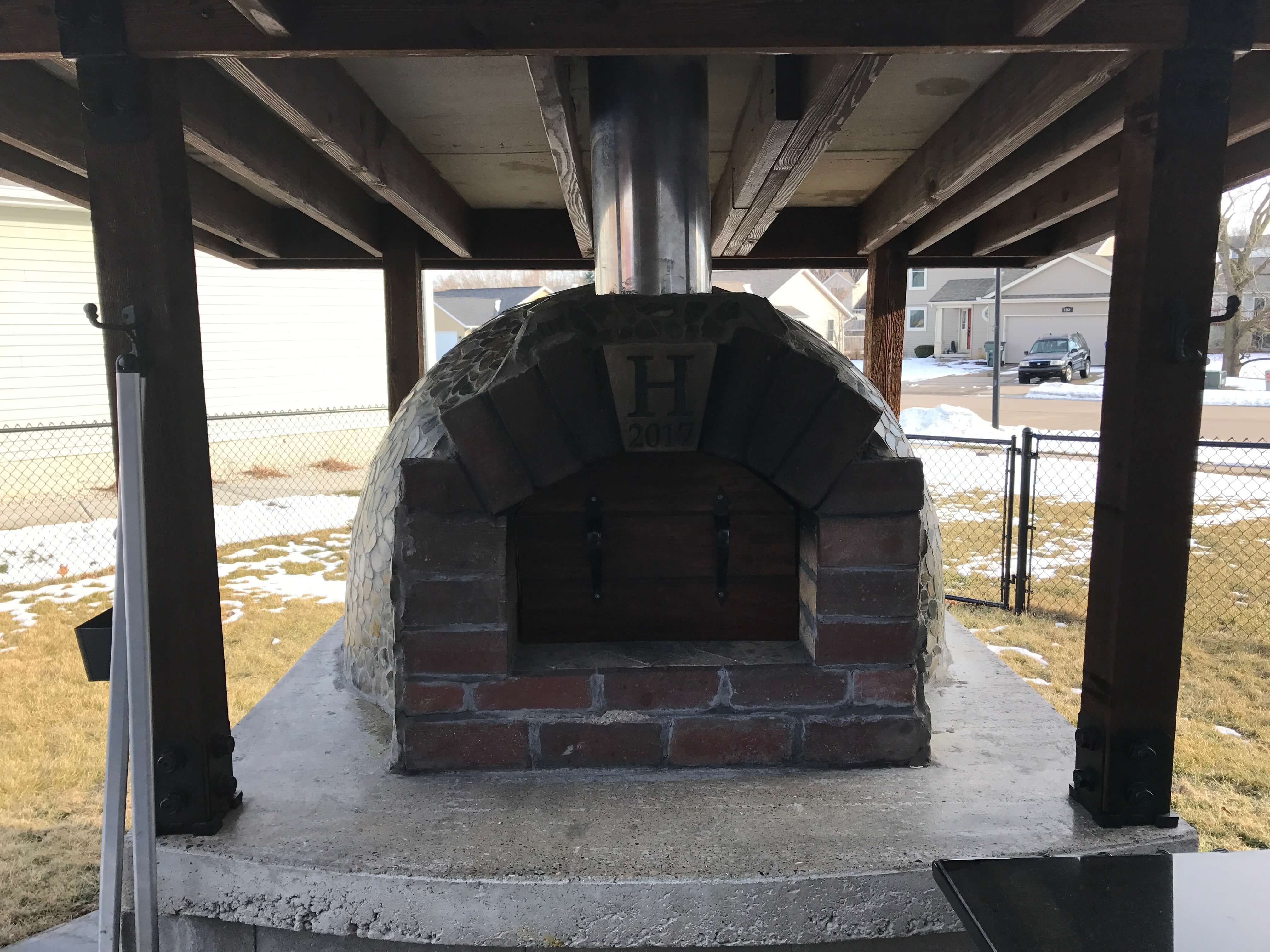Custom igloo-style pizza oven with brick front under a roof structure