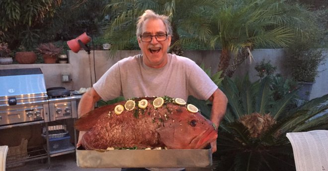 Man smiling broadly holding a 28 lb Pink Grouper ready to go in a wood fired oven