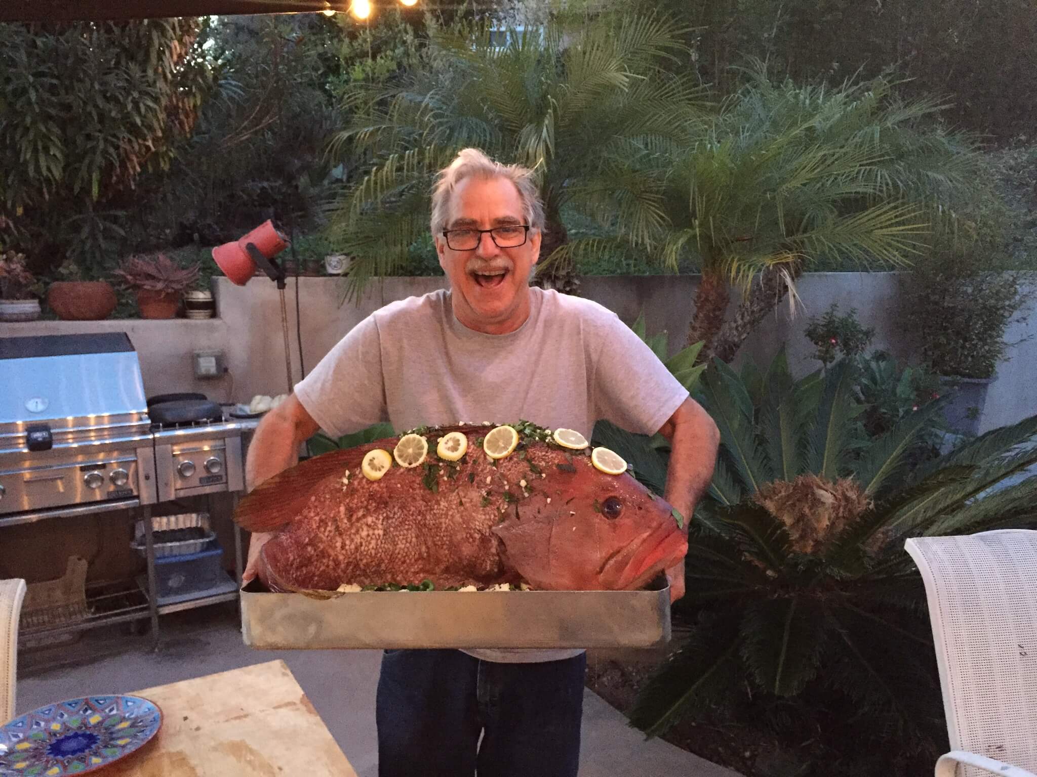 Man smiling broadly holding a 28 lb Pink Grouper ready to go in a wood fired oven