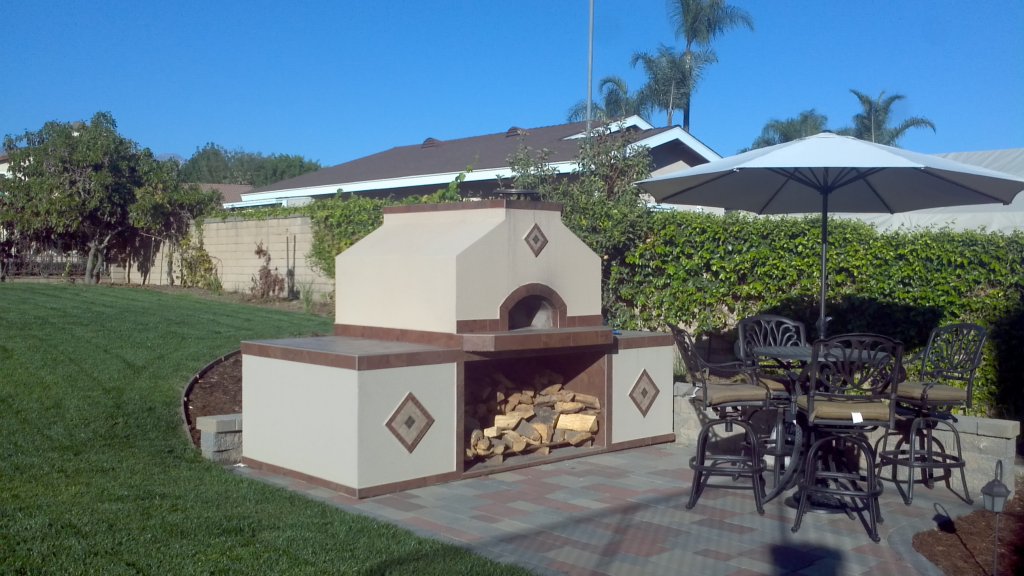 Outdoor patio and lawn with gabled cream colored stucco Casa 110 pizza oven - round table and umbrella