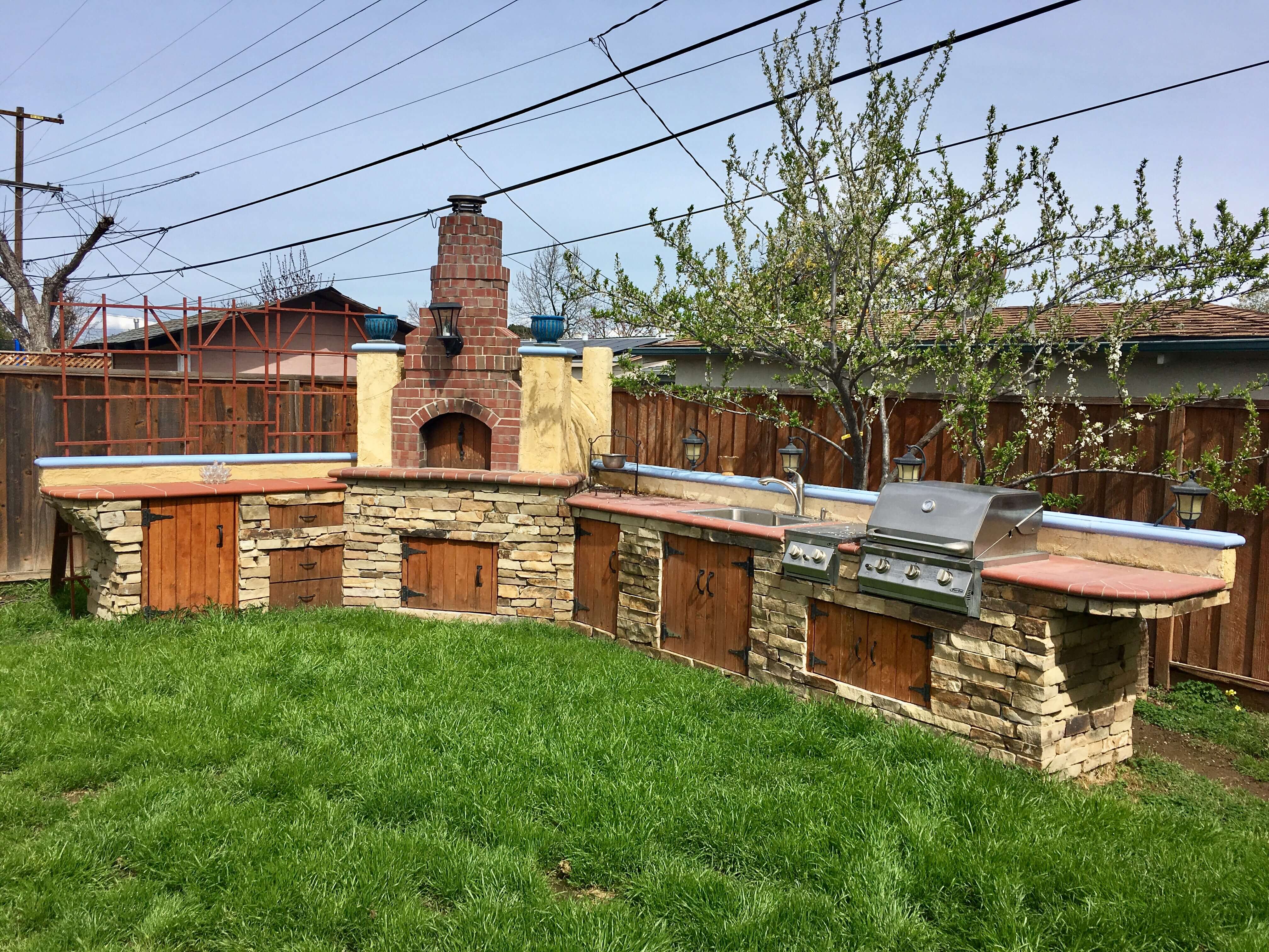 Outdoor kitchen and brick pizza oven made with mixed materials of stone red brick stucco terracotta wood and steel