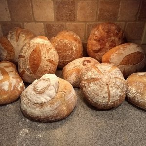 Pile of Round Loaves of Wood Fired Sourdough Bread on a Counter against a Brick Back Splash