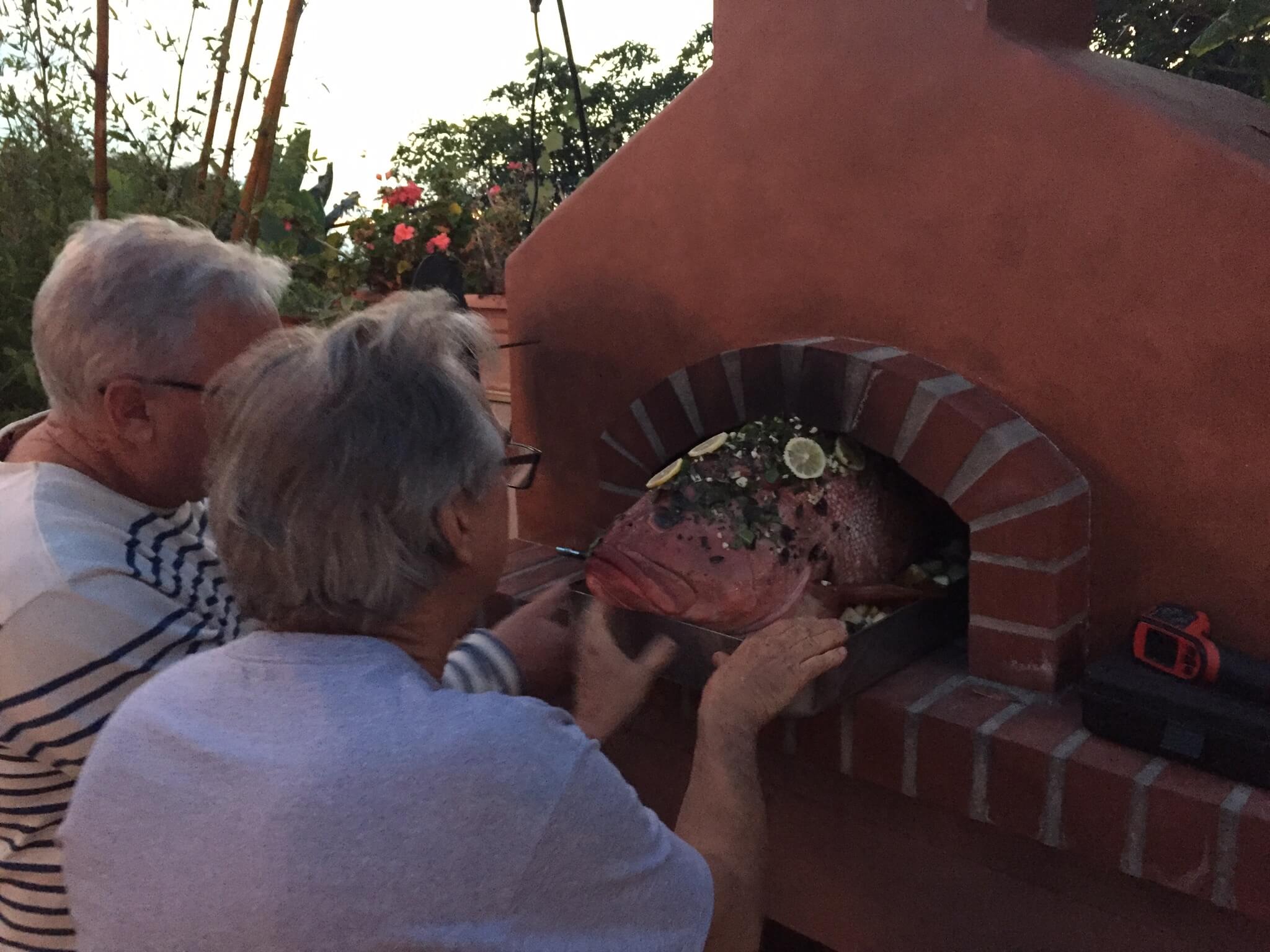 Two men easing a 28lb Pink Grouper into a Toscana pizza oven with zero inches to spare