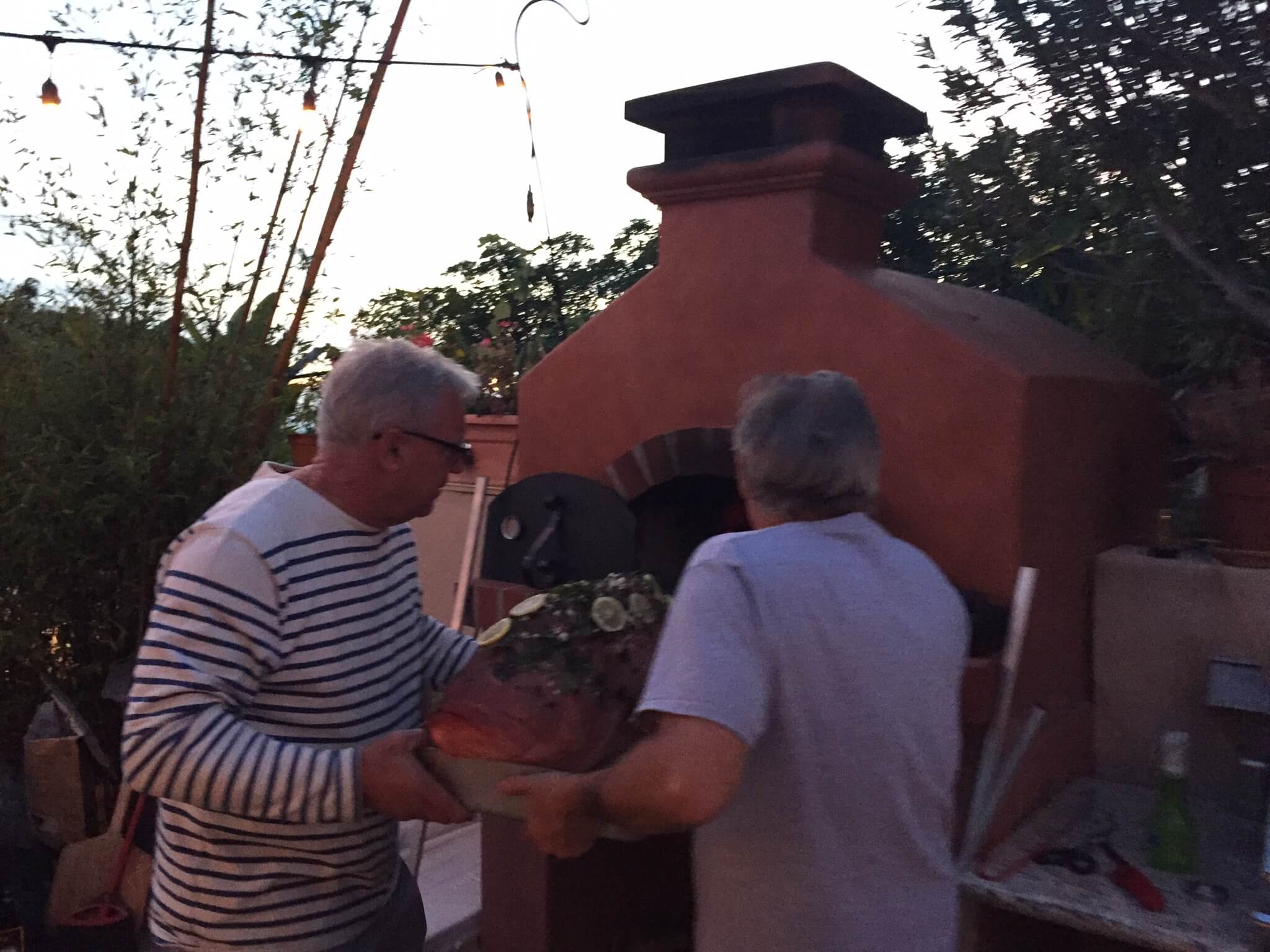 Two men trying to put a 28lb Pink Grouper into a Toscana pizza ove