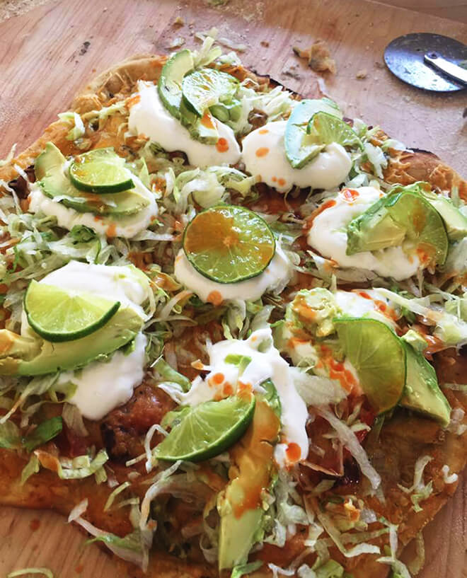 Pizza topped with pancetta-shrimp-vegetables-lettuce-lime_crema-lime_slices-avacado