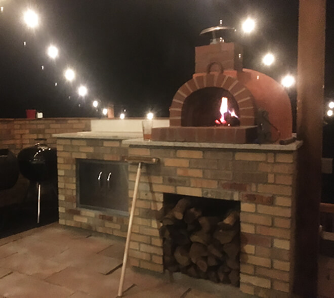 Red Stucco Finished Giardino Pizza Oven on counter at night - patio lights