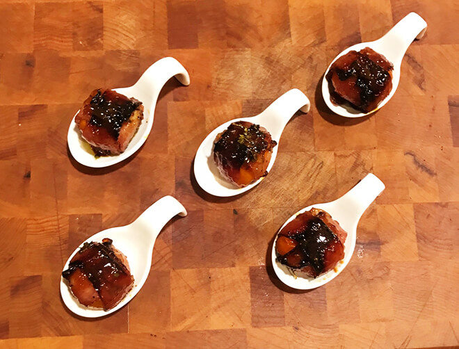 Wrapped peppers plated in serving spoons on a butcher block