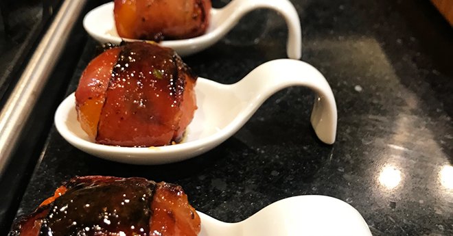 Row of ham-wrapped baked peppers in white serving spoons