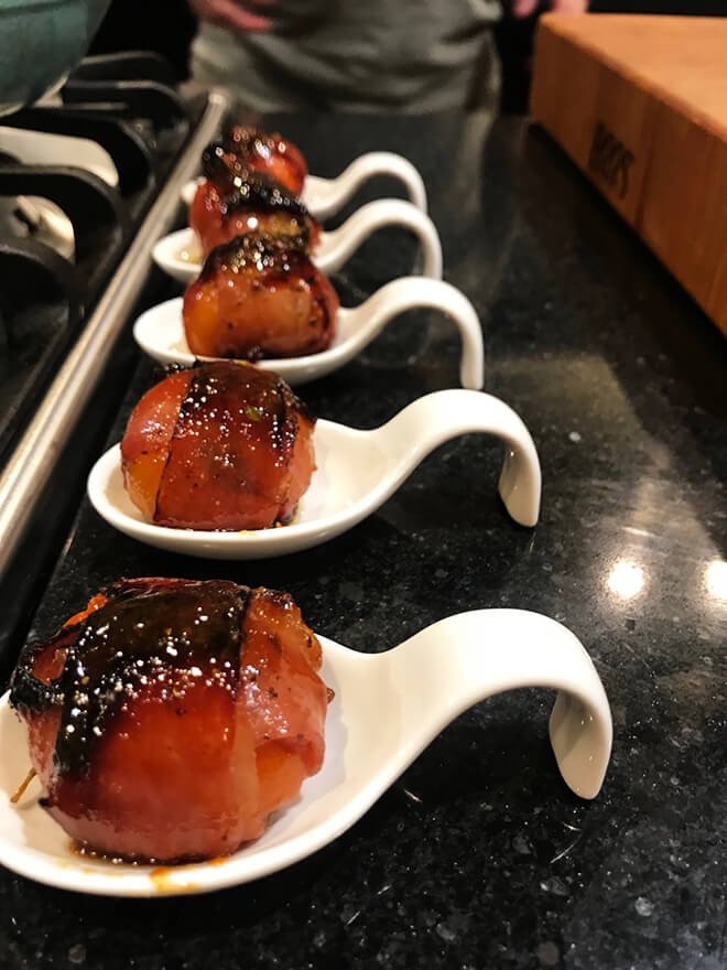 Row of ham-wrapped baked peppers in white serving spoons