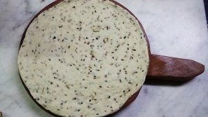 Wooden Eid Bread Mold covered in white dough with dark seeds