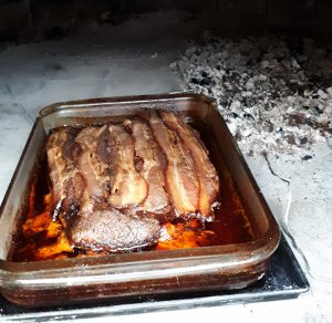 Pyrex pan with bacon covered brisket in wood fired oven