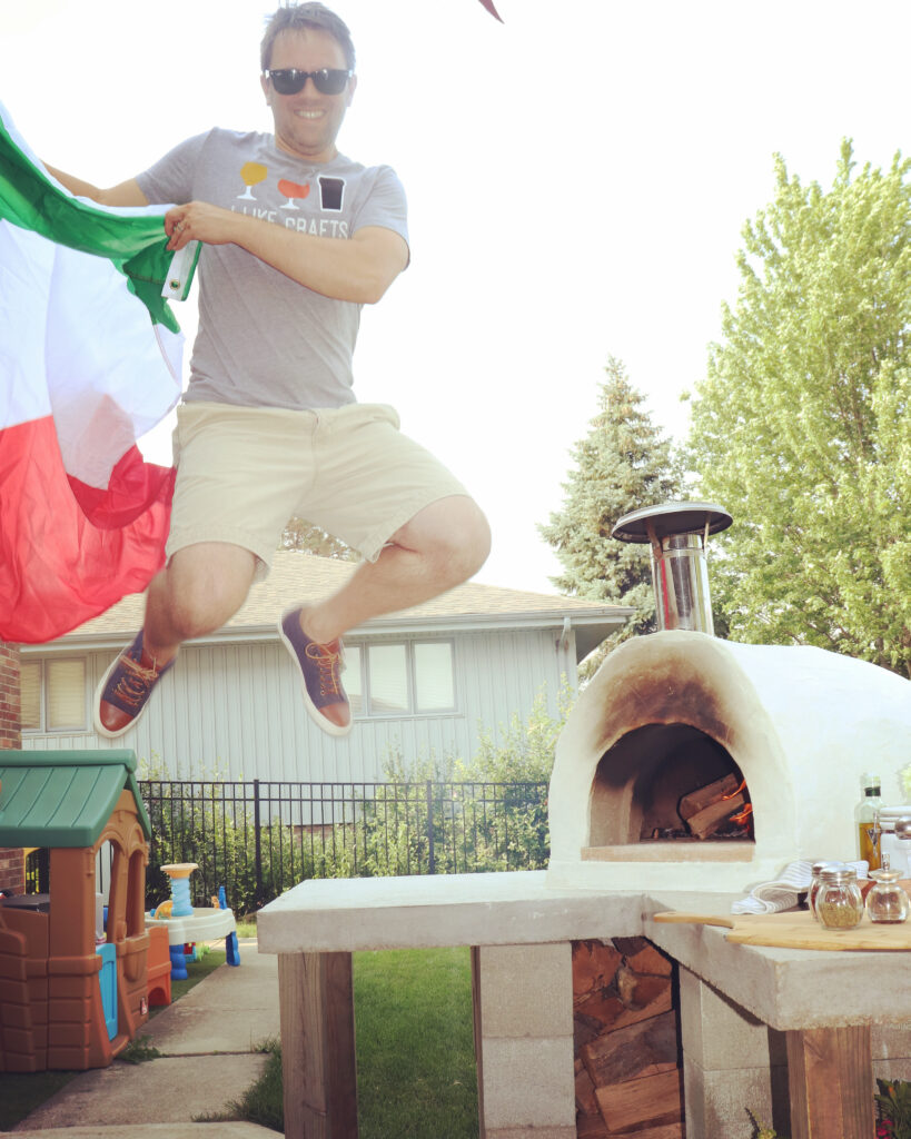 man jumping-holding italian flad-pizza oven