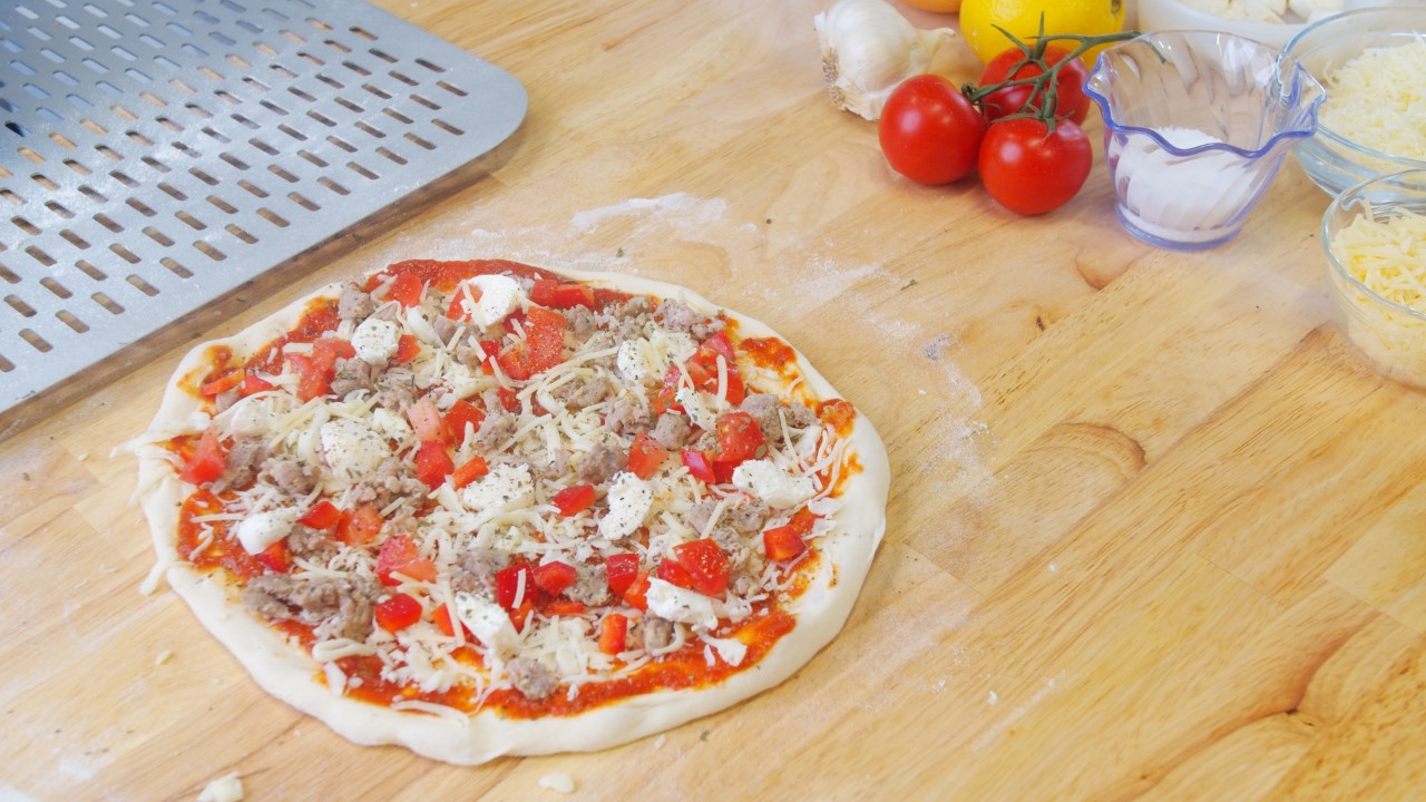 Sausage adn ared pepper pizza on coubter before cooking